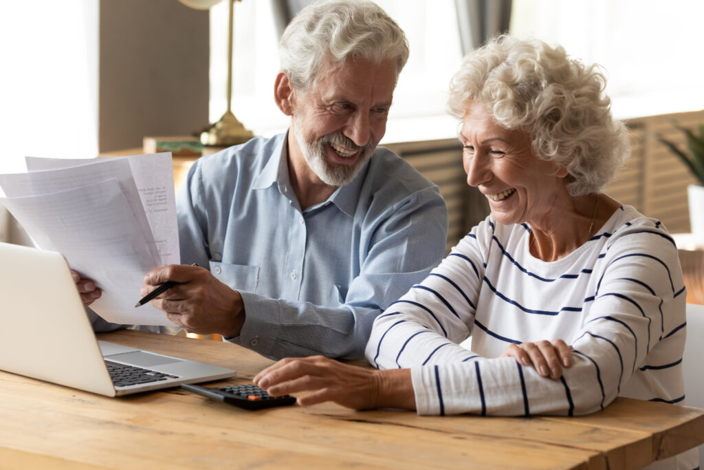 Senior couple looking at laptop and paperwork smiling
